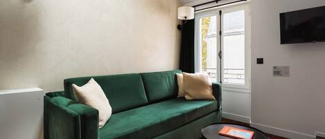 Un salon moderne avec un canapé vert, une table basse ronde noire et un téléviseur à écran plat fixé au mur.