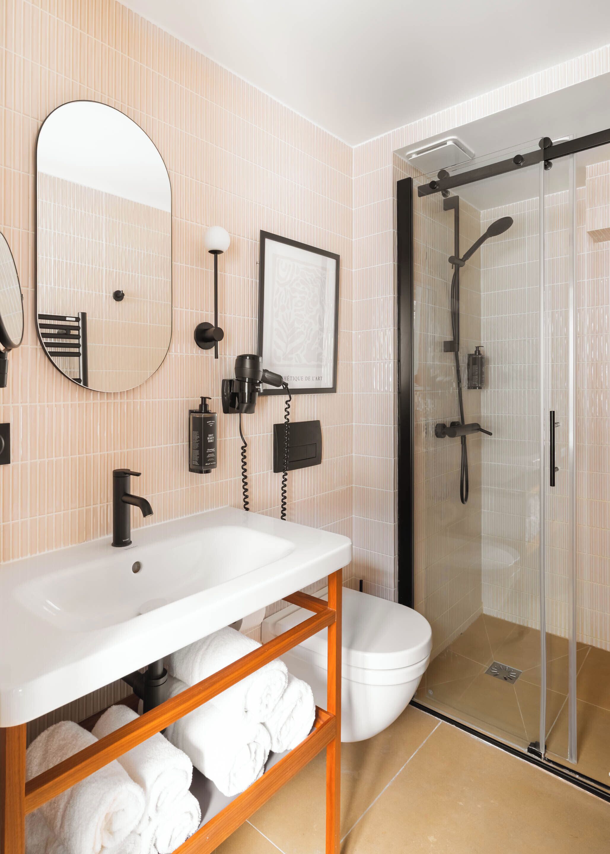 Een moderne badkamer met een witte wastafel, een spiegel, een kunstwerk in een lijst, een haardroger en een douche met glazen wanden.