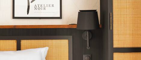 A hotel room with a bed, a framed artwork on the wall, a bedside lamp, and a small table with books.