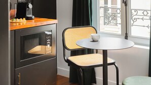 Et lille værelse med et bord, en stol, en kaffemaskine og et vindue med gardiner.