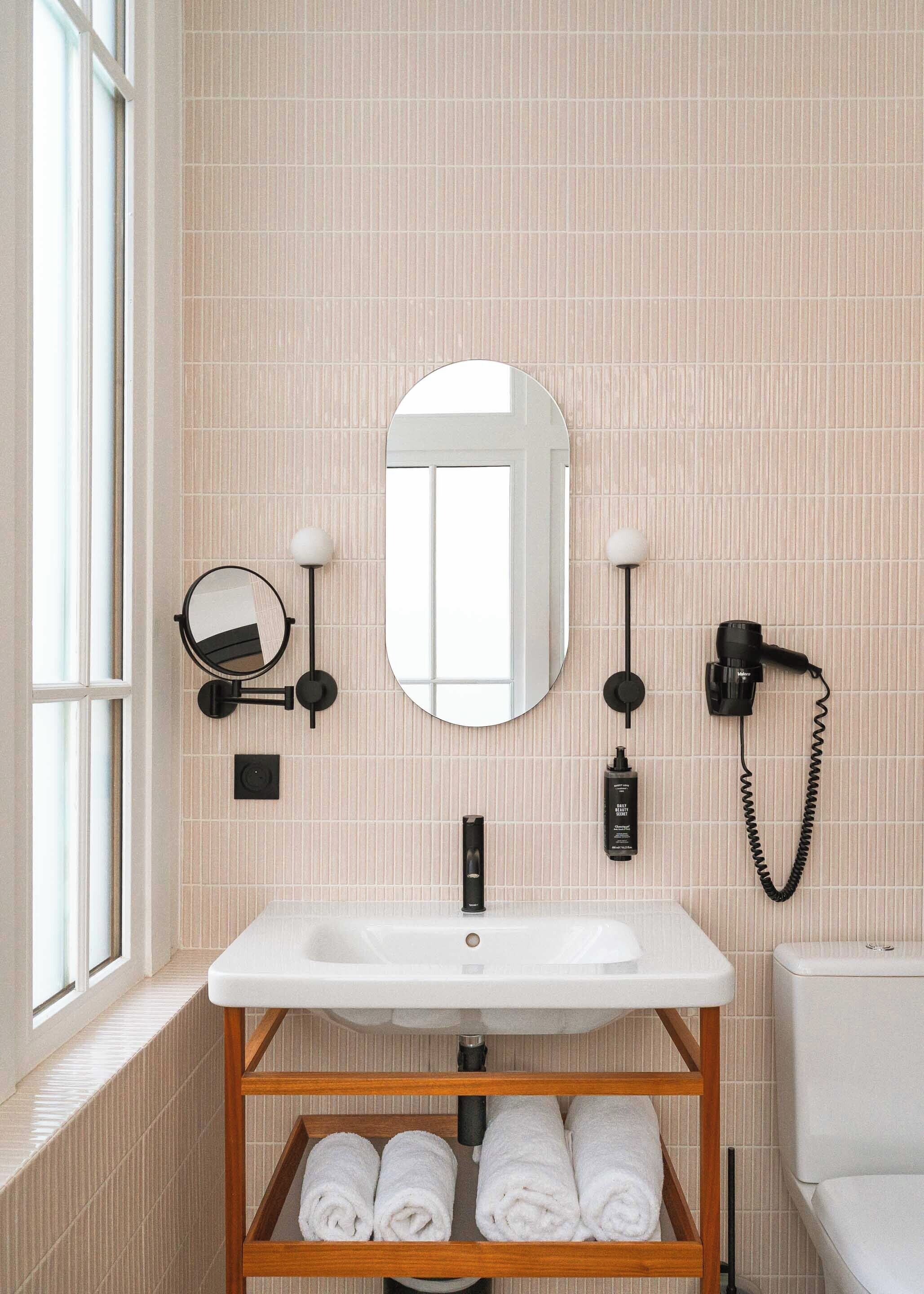 Une salle de bain avec un lavabo blanc, un miroir, un sèche-cheveux et une étagère avec des serviettes.
