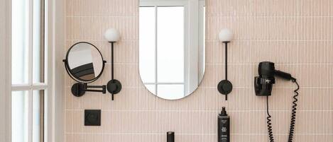 Une salle de bain avec un lavabo blanc, un miroir, un sèche-cheveux et une étagère avec des serviettes.