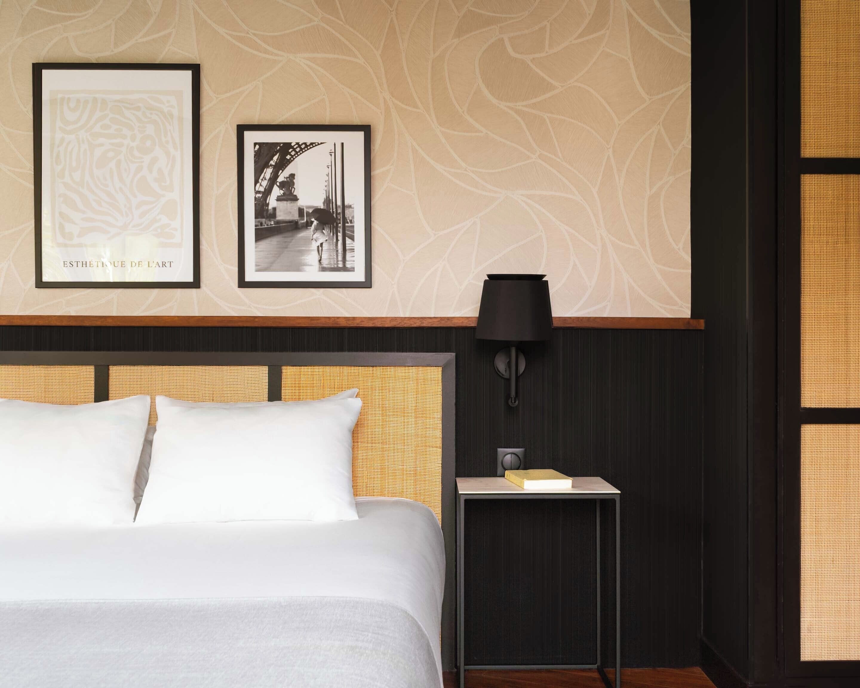 A hotel room with a bed, a nightstand, a lamp, and two framed pictures on the wall.