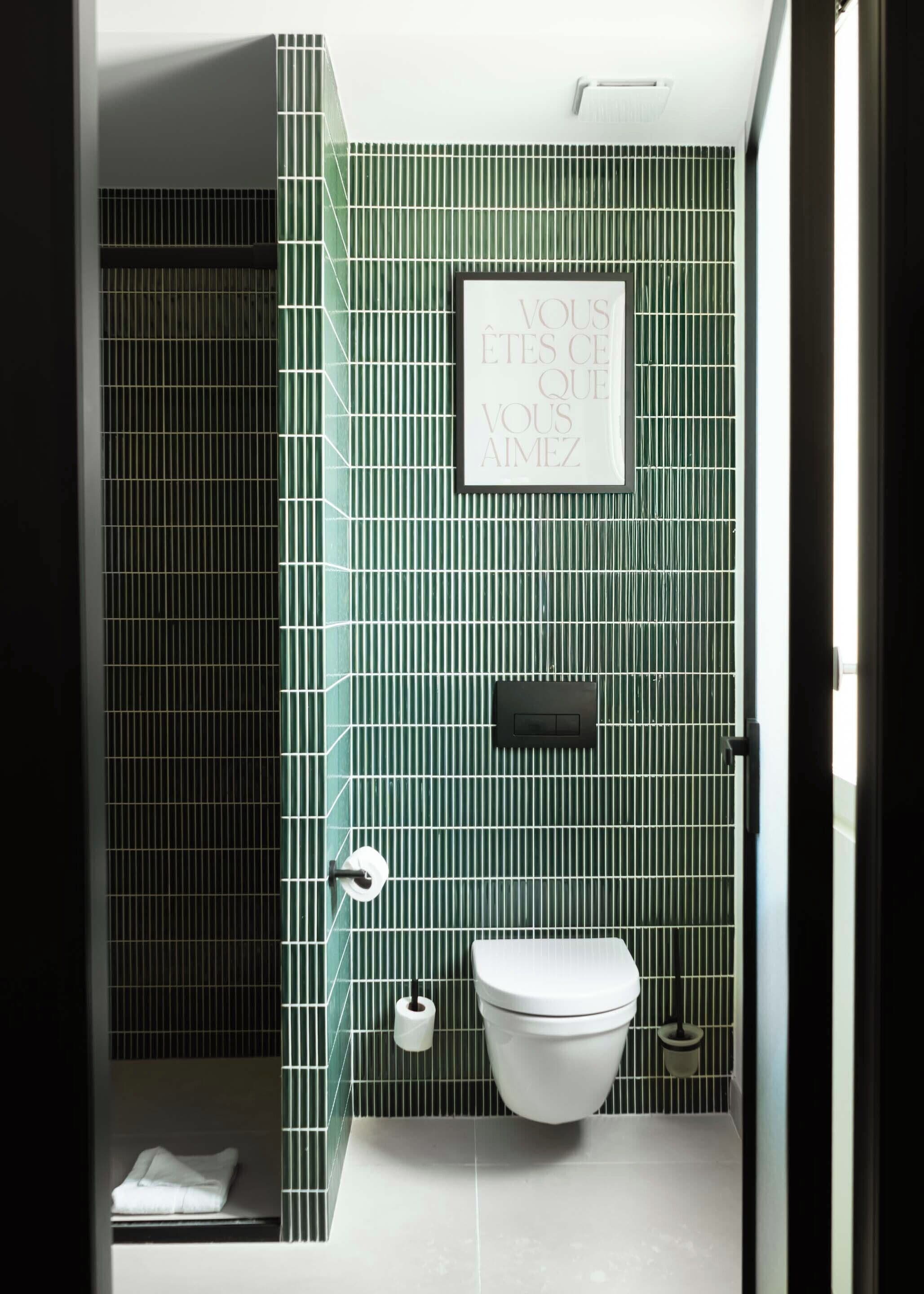 A bathroom with green vertical stripes on the walls, a framed sign above the toilet, and a towel rack with a roll of toilet paper.
