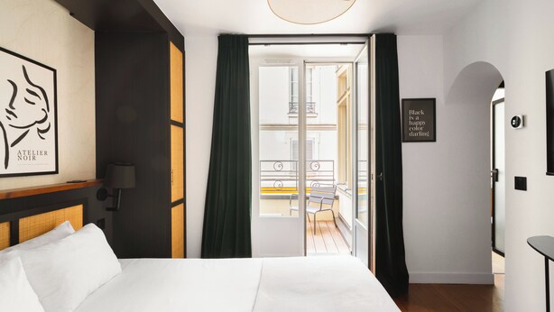 Et hotelværelse med en seng, udsigt til en balkon, en dør med et skilt og en væg med et indrammet billede.