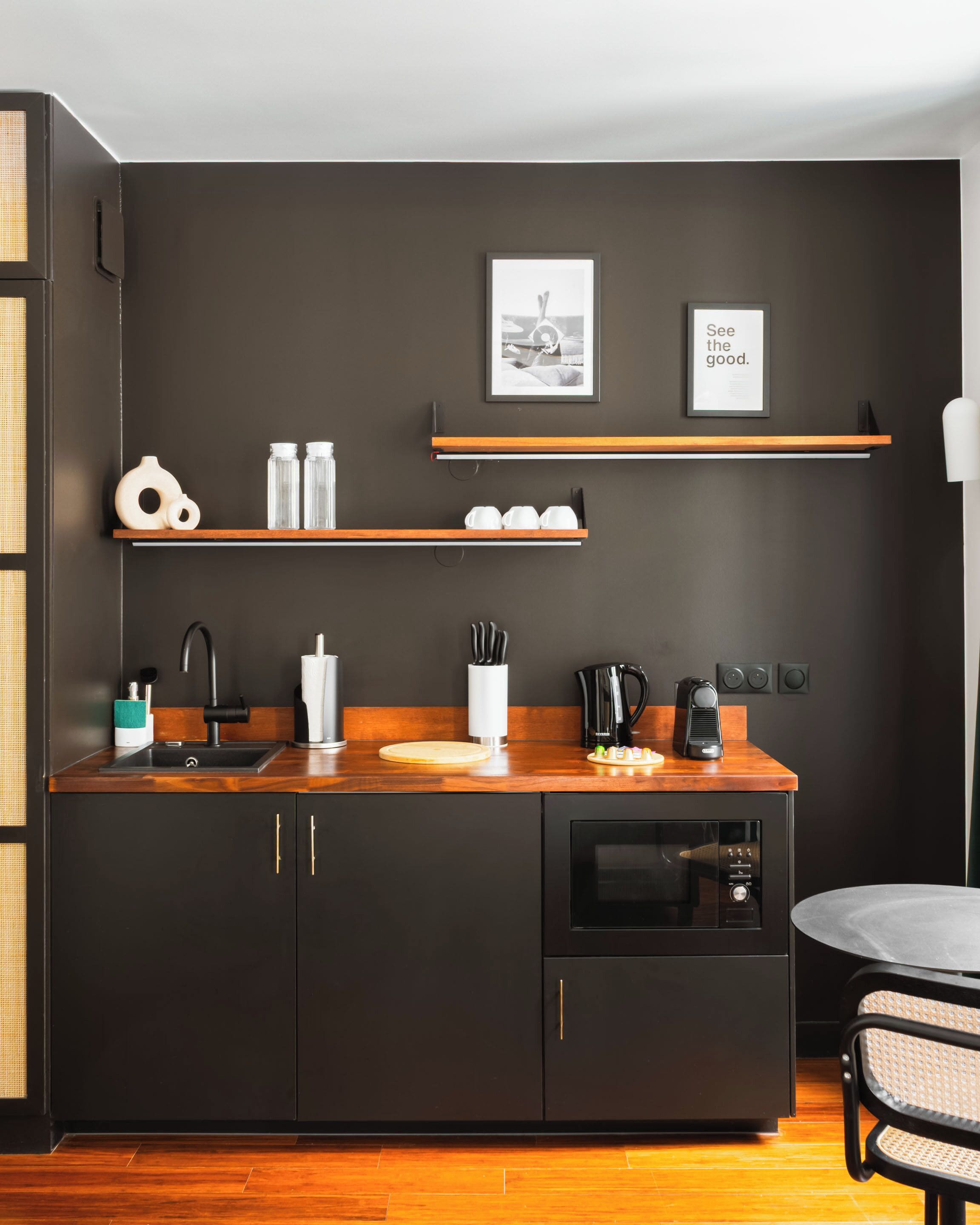 A modern kitchen with dark cabinetry, a wooden countertop, a built-in oven, and a coffee machine.