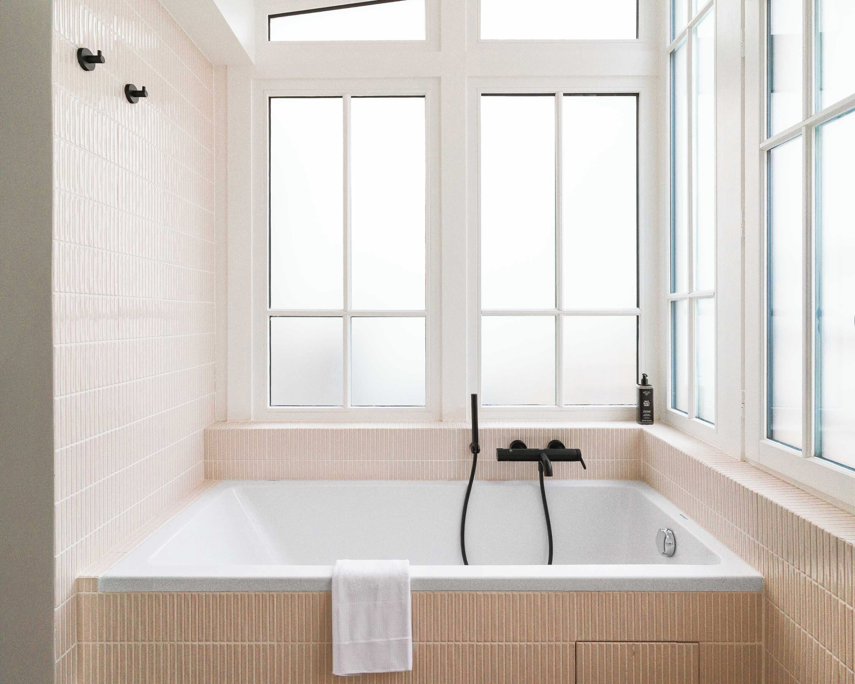 A modern bathroom with a freestanding bathtub, two black towel rings, and large windows providing natural light.