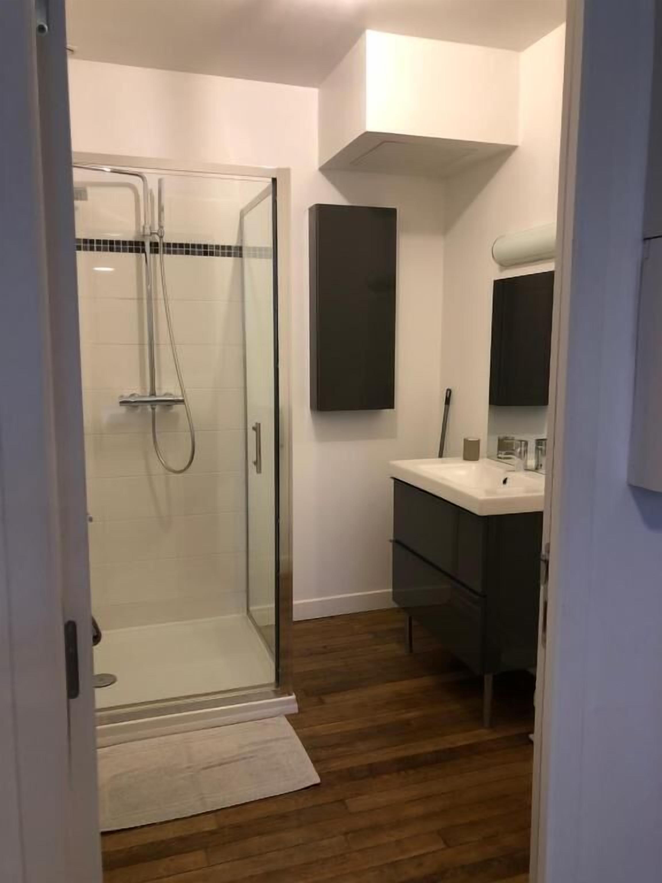 A modern bathroom with a glass shower enclosure, a dark vanity, and a white sink.