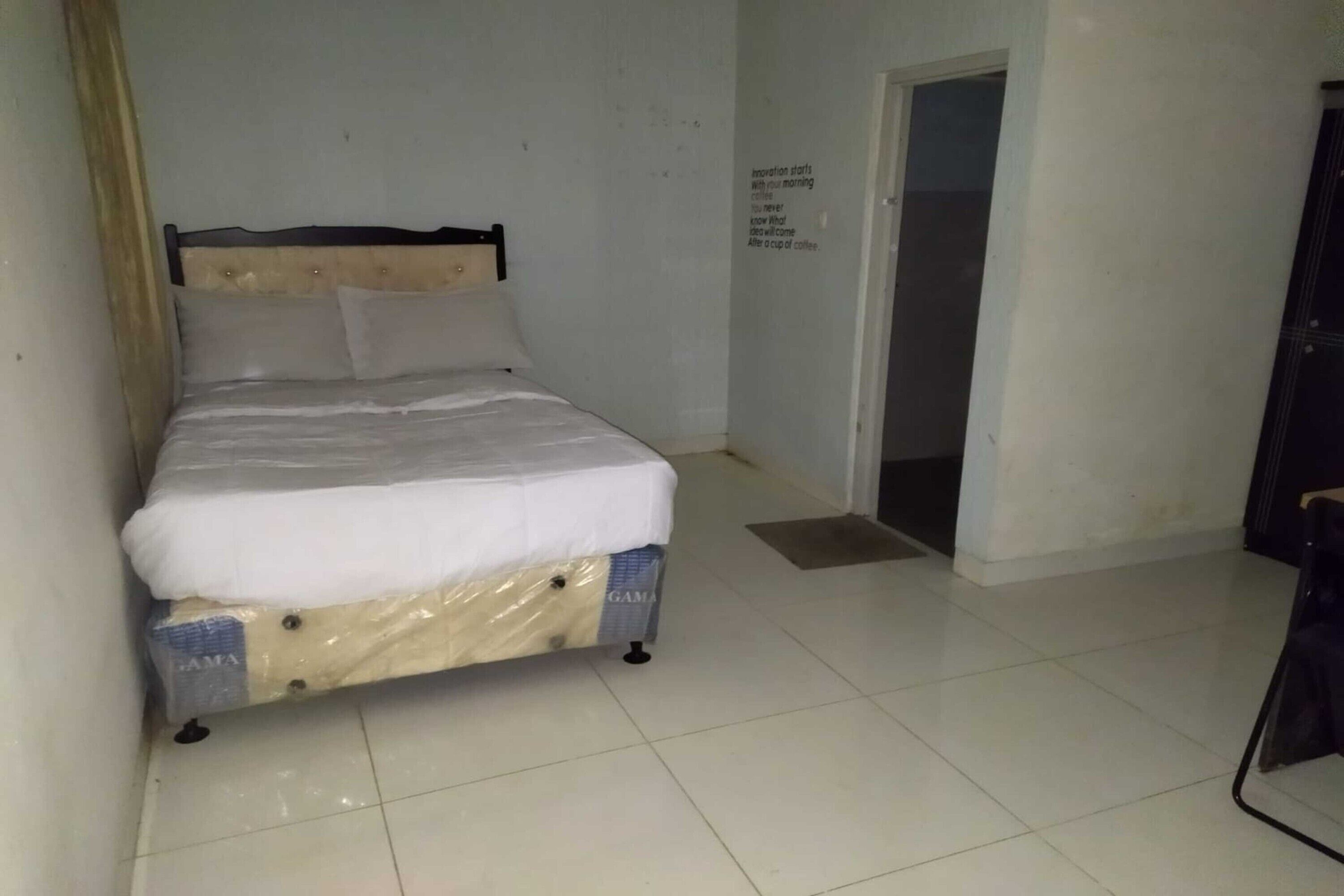 A small, clean room with a single bed, a door, and a wall with a motivational quote.