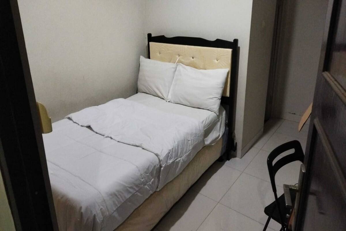 Une petite chambre avec un lit simple, une tête de lit en bois et du linge de lit blanc.