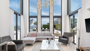 Amplia sala de estar con ventanas grandes, una lámpara moderna y vistas al exterior.