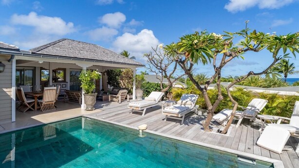 Un espace aménagé au bord de la piscine, avec des chaises longues, un coin salon abrité et une vue sur l’océan.