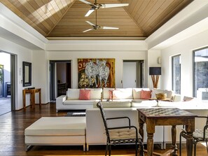 Relax in this stylish living room with a high ceiling, featuring a large sofa, a chessboard, and a beautiful abstract art piece.