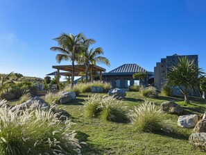 Relax in a shaded outdoor space under a wooden roof, surrounded by lush tropical plants and grasses.