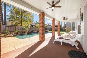 A covered patio with a pool, brick pillars, ceiling fans, and lounge chairs.