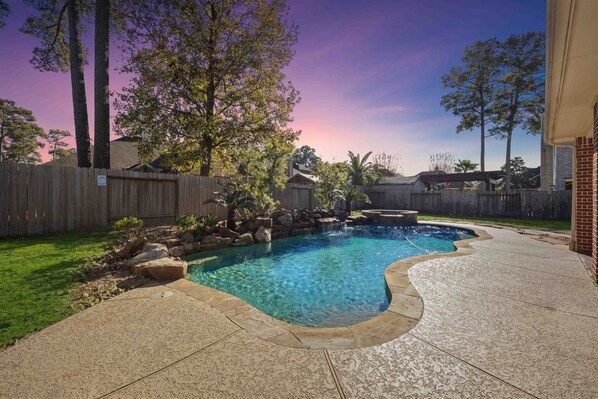 A backyard with a swimming pool, a wooden fence, and a brick patio.