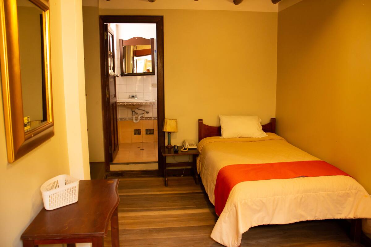 A hotel room with a bed, a nightstand, a lamp, a telephone, and a mirror.