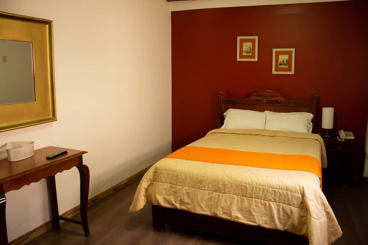 A hotel room with a wooden bed, a bedside table with a lamp, and two framed pictures on the wall.