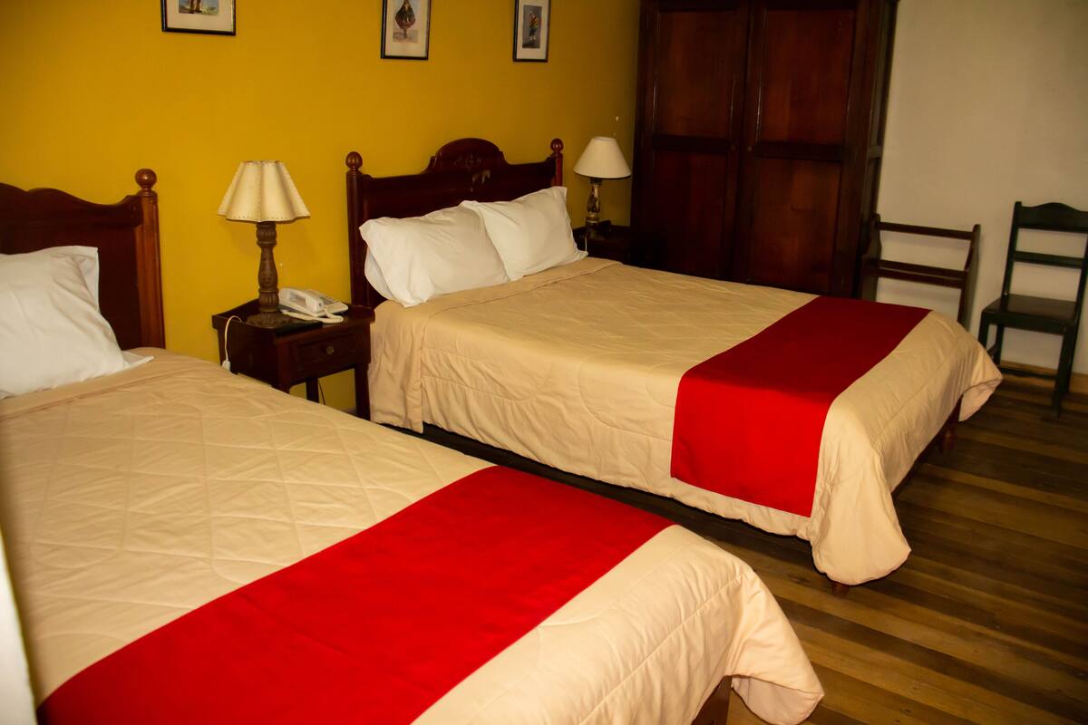 Two beds with red bedspreads in a room with wooden flooring and yellow walls.