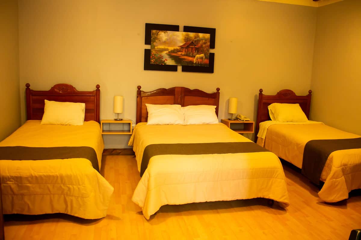 A hotel room with three single beds, wooden headboards, and a painting on the wall.