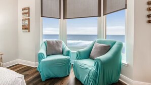 A room with two teal armchairs facing a large window overlooking the ocean.