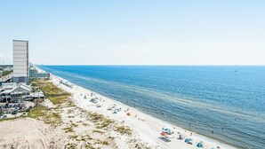 A beach with a high-rise building, sandy shore, and clear blue sea.
