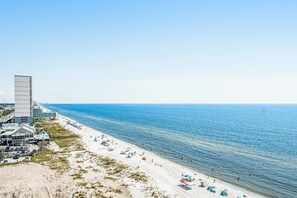 Ein Strand mit einem Hochhaus, sandigem Ufer und klarem, blauem Meer.