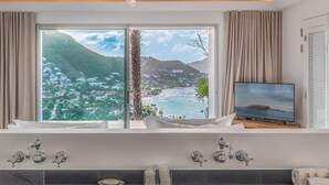 Une salle de bain moderne avec une baignoire, une grande fenêtre offrant une vue panoramique et un téléviseur posé sur un meuble.