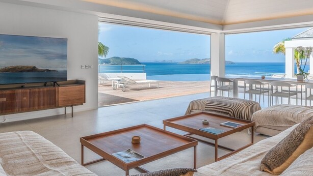 Un salon moderne doté d’un grand téléviseur, d’un canapé, de deux tables basses et offrant une vue sur la mer.