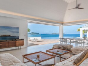 Ein modernes Wohnzimmer mit großem Fernseher, einer Couch, zwei Couchtischen und Meerblick.