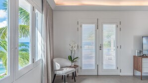 Une chambre moderne avec de grandes fenêtres, une chaise blanche, une petite table et un téléviseur posé sur un meuble en bois.