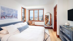A bedroom with a large bed, a view of mountains through a window, a wooden chair, a round mirror, and a dresser with a vase. - 15 Aspen Ridge-Curate Telluride-Ski In/Out, Hot Tub, Firepit, Walk to Gondola (Mountain Village)
