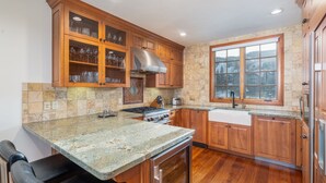 A kitchen with wooden cabinets, granite countertops, a stainless steel range hood, and a window providing a view of the outside. - 15 Aspen Ridge-Curate Telluride-Ski In/Out, Hot Tub, Firepit, Walk to Gondola (Mountain Village)