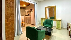 Una sala de estar moderna con una pared de ladrillo decorativa, un sillón verde, una mesita y una cocina al fondo.