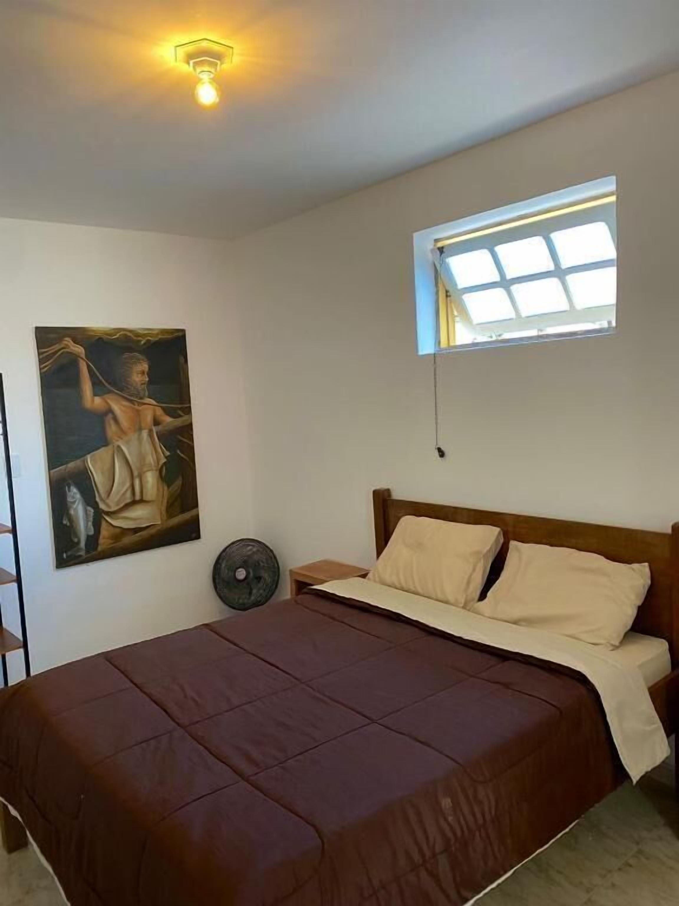 Et soveværelse med en seng, et vindue, en loftslampe og et billede på væggen.