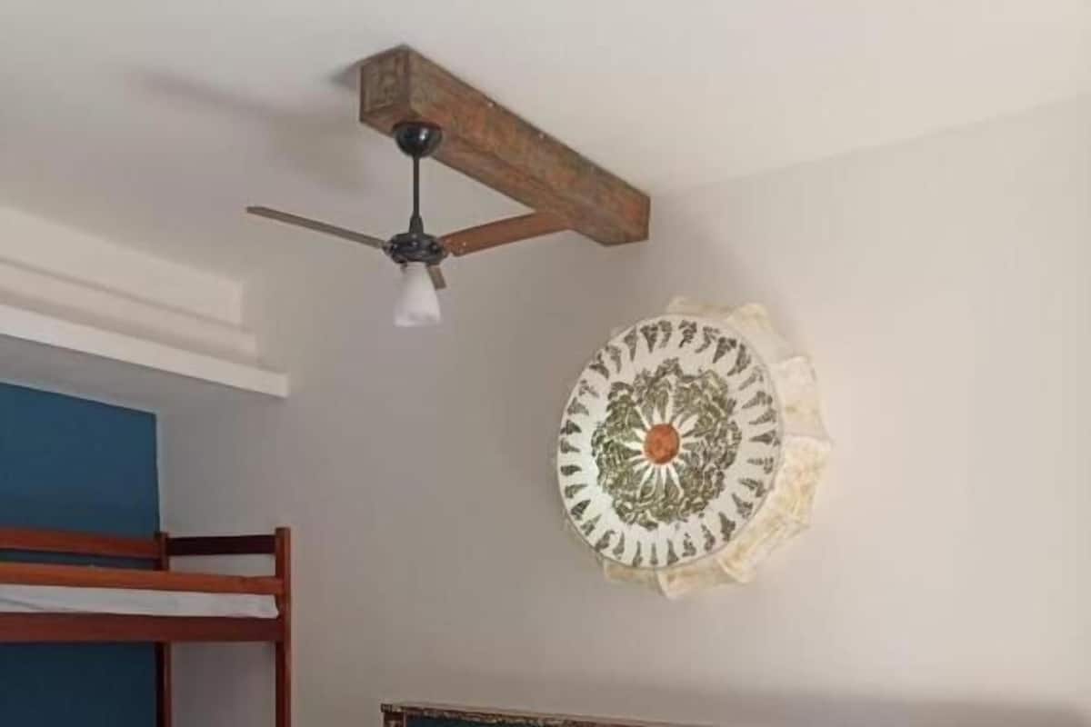 Une chambre avec un lit superposé, un lit simple avec une literie blanche, un élément décoratif mural et un ventilateur de plafond.
