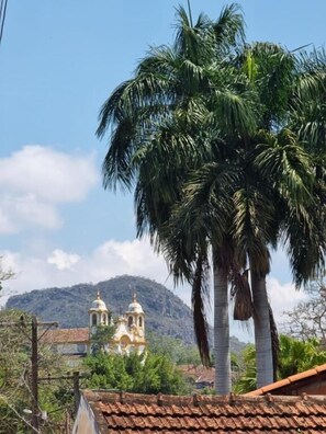 A view of a church with two bell towers, surrounded by palm trees and a mountain in the background. - Hospedagem Central (Tiradentes)