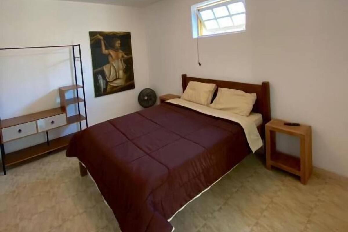 Une chambre à coucher avec un lit, une petite table, une étagère, un tableau et une fenêtre.