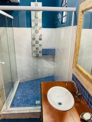 A bathroom with a glass shower enclosure, a white sink, and a blue-tiled floor. - Hospedagem Central (Tiradentes)