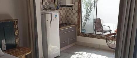 Un dormitorio con cama, una kitchenette pequeña y un balcón con una silla.