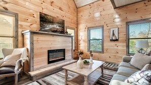 L’intérieur chaleureux d’un chalet avec une cheminée, des murs en bois, un canapé et une table basse.
