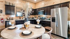 Une cuisine moderne avec un lambris en bois, des appareils électroménagers en acier inoxydable et une table de salle à manger ronde, dressée pour quatre personnes.