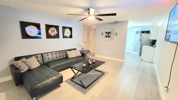 A modern living room with a black leather sofa, a glass coffee table, and a ceiling fan.