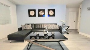 A modern living room with a sectional sofa, a glass coffee table, and three wall-mounted flower paintings.