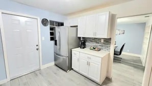 A compact kitchen with white cabinets, a stainless steel refrigerator, and a coffee maker.