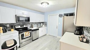 A modern kitchen with white cabinets, a stainless steel microwave, a gas stove, and a refrigerator.