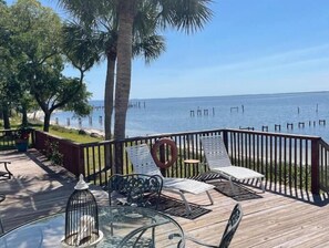 A wooden deck with outdoor furniture, including chairs and a table, overlooking a body of water with a clear sky. - Coastal Adventures Waterfront! (Carrabelle)