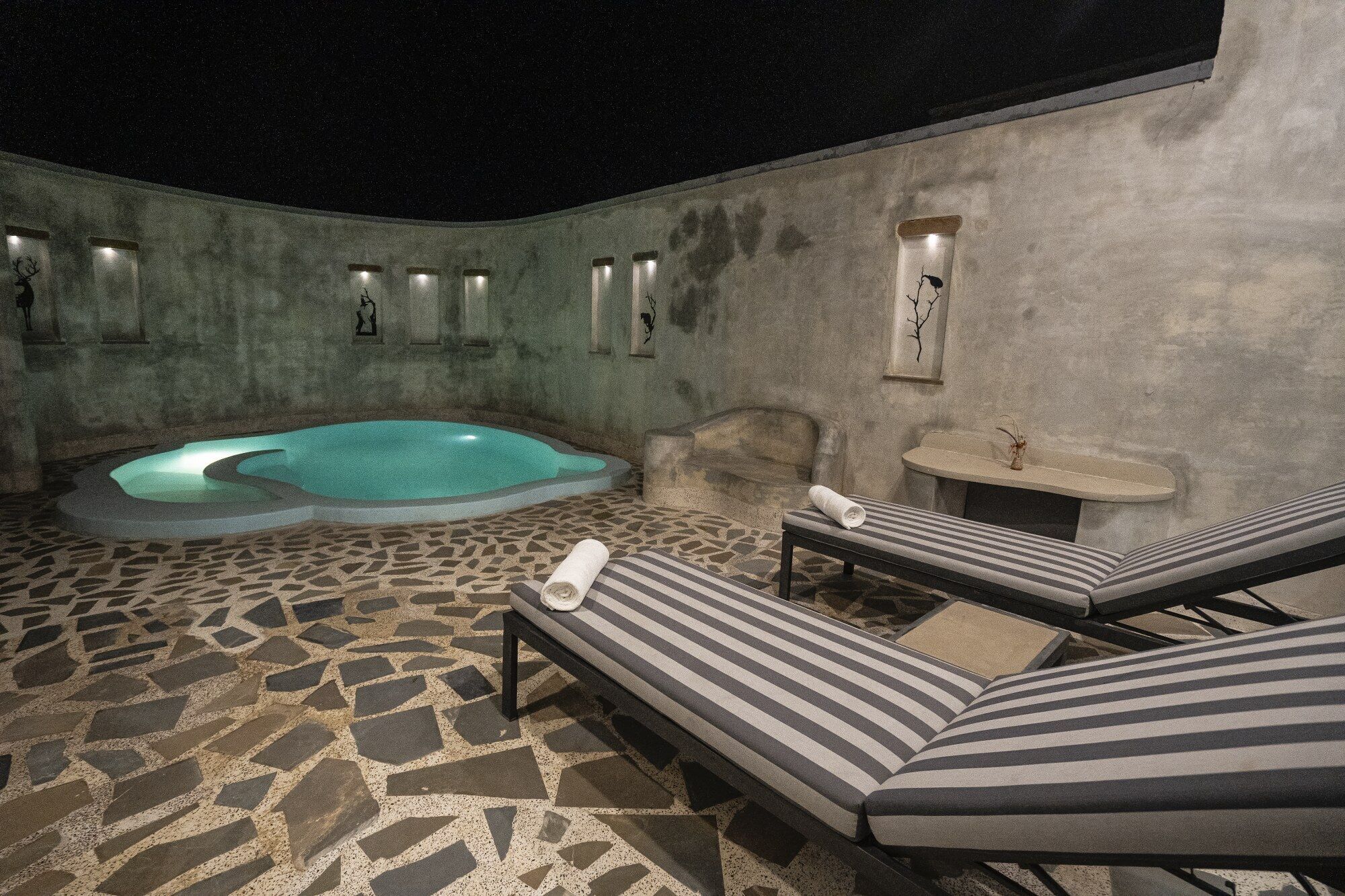 Un espace spa comprenant un bain à remous, des chaises longues et un sol carrelé en pierre.