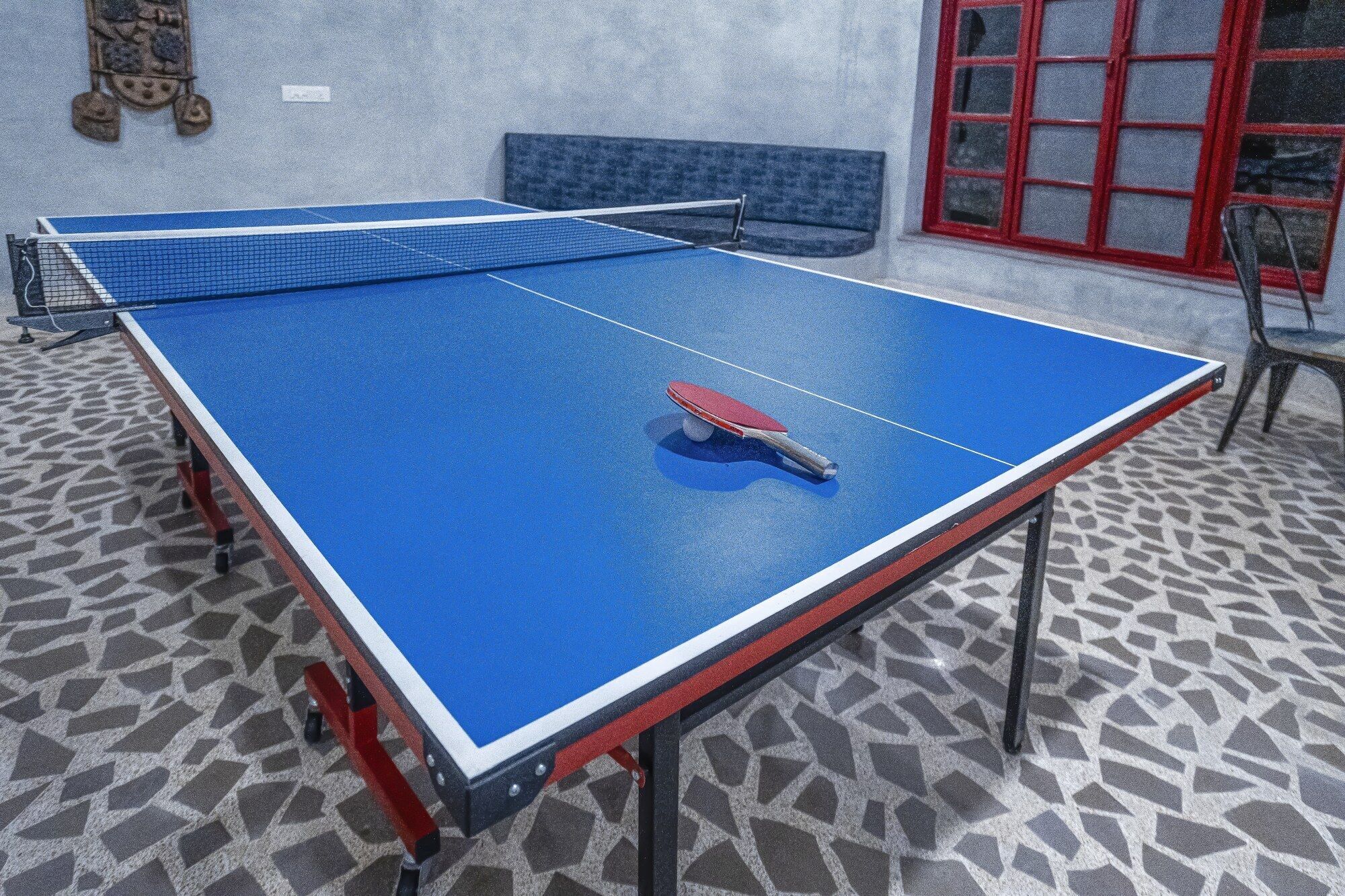 A ping pong table with a red paddle in the center, set against a patterned floor.