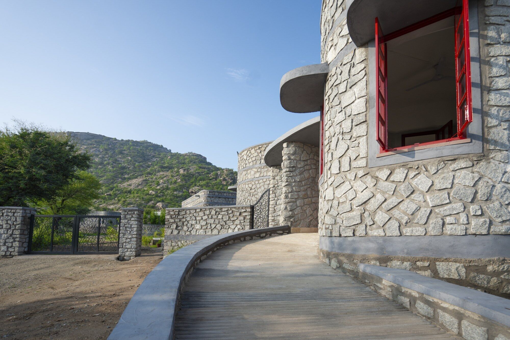 A stone building with a curved pathway leading to a red-framed window.